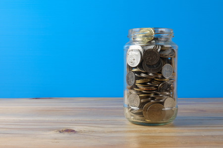 Mason jar with coins over blue back drop. Finance and saving concept.