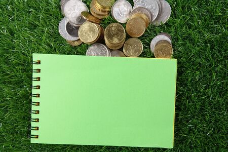 Coins and notepad on the green background.の写真素材