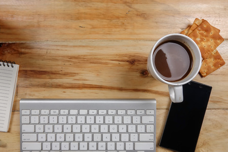 Keyboard,smartphone,notepad,pen,biscut,coffee and green plant on the wooden table. Top view.の写真素材
