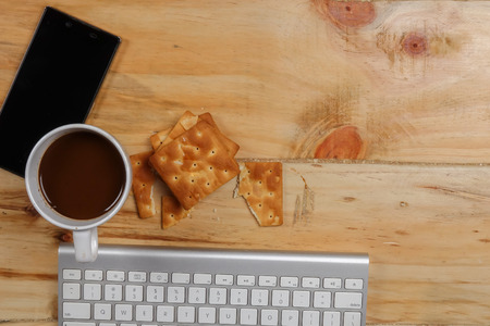 Keyboard,smartphone,notepad,pen,biscut,coffee and green plant on the wooden table. Top view.の写真素材