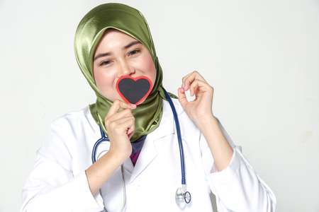 Smiling female doctor holding heart shape  studio portrait isolated on white backgroundの写真素材