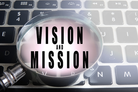 Magnify glass and coins on keyboard with VISION AND MISSION text. Business  concept.