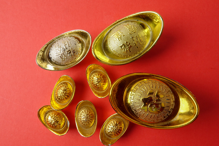 Gold ingots for Chinese New Year festive decorations on a red background. Chinese character means luck,wealth and prosperity as seen in the image.の写真素材