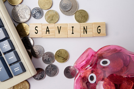 SAVING CONCEPT. Red piggy bank and coins with word SAVING on wooden plates.の写真素材