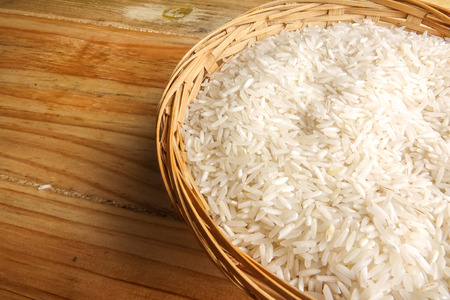 Fresh rice in wicker basket over a wooden table. Side lighting effect.の写真素材