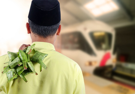 Eid Mubarak concept: Man standing waiting for train with holding a bundle of coconut rice dumpling.の写真素材