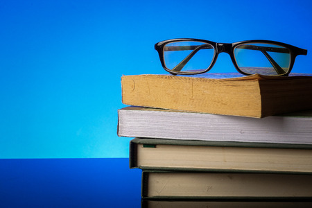 EDUCATION CONCEPT with stack of old book and reading glasses on a blue background.