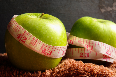 HEALTH LIFESTYLE CONCEPT: Green apples and measuring tape over black rustic background. Selective focus.の写真素材