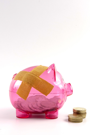 SAVING  DETERIORATE CONCEPT. Red piggy bank with bandage and small stack of coins.の写真素材