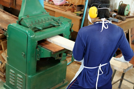 Worker is working with planing of wood machine.He is wearing safety equipment in factory, Top viewの写真素材