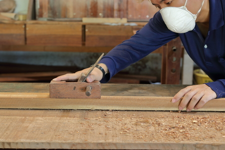 Carpenter working with a hand planer on  a plank of wood in carpentry workshop. He is wearing safety equipment .の写真素材