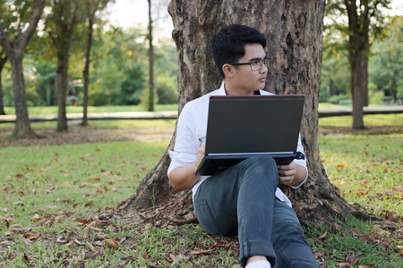 Portrait of handsome young man sitting on a green grass with laptop in the park.の写真素材