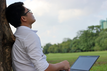 Resting time. Asian young man looking at the sky after work against his laptop.の写真素材