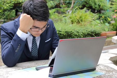 Portrait of handsome businessman looking at laptop and thinking about his job in the park outdoorsの写真素材