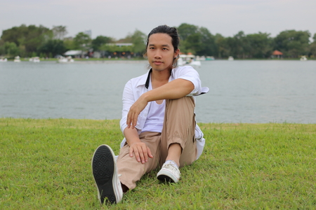 Portrait of young Asian man sitting on a green grass in nature river relax timeの写真素材