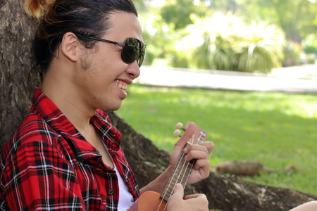 Young man playing ukulele in the park outdoor. He is smilingの写真素材