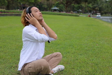 Portrait of a young man resting with headphones in the park outdoorsの写真素材