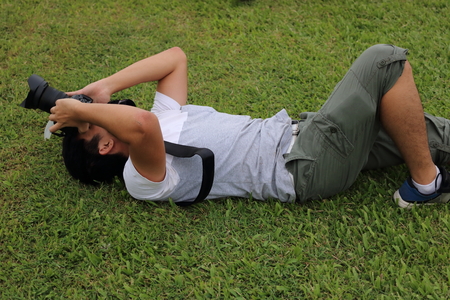 Young man photographer lying on green grass ground with holding camera dslr in the hands.