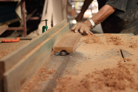 Selective focus and shallow depth of field. A piece of wood is being shaved on a router table by hands of carpenter in carpentry workshop.の写真素材