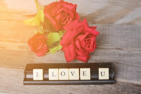 I love u wording by crossword on old wooden board with artifical roses background. Sunshine effect. Love and romance Valentine's day concept.の写真素材