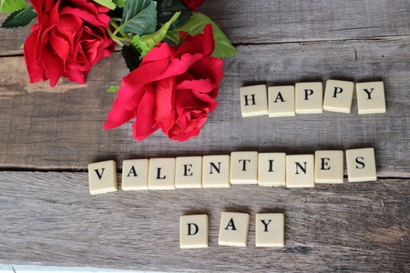 Crossword puzzled with blocks spelling happy valentines day words on old wooden board with artificial red roses background.の写真素材
