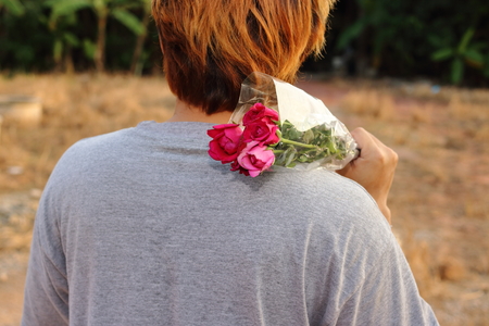 Young man holding a beautiful bouquet of red roses over shoulder on nature blurred backgroundの写真素材