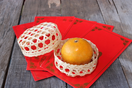 Orange in a basket on old wooden board with Chinese red envelope packet or ang pao background. Happy Chinese new year concept.の写真素材
