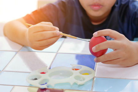 Hands of cute boy painting  egg with paintbrush for preparing Easter day. Sunshine effectの写真素材