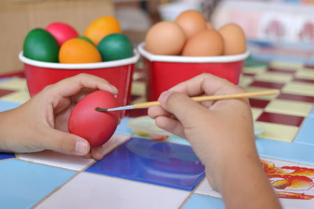 Selective focus and shallow depth of field. Easter eggs are painted with paintbrush by little boy.の写真素材
