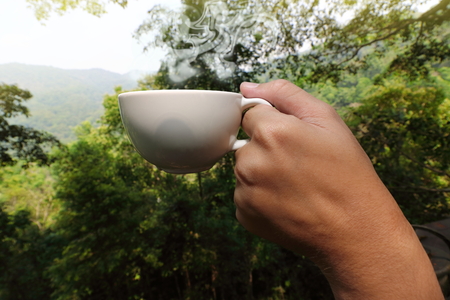 Close up hands of young tourist holding coffee cup  in beautiful morning nature background.の写真素材