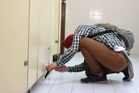 Masked thief with a balaclava sneaking and taking a photo with mobile smart phone in toiletの写真素材