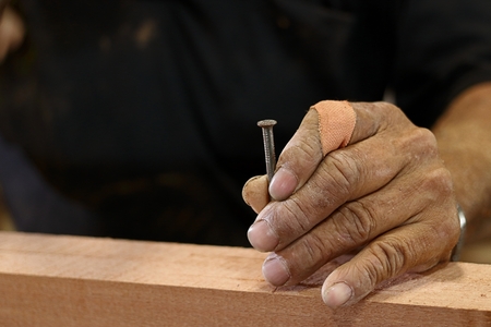 Hands senior carpenter holding nail on wooden piece with copy space.の写真素材