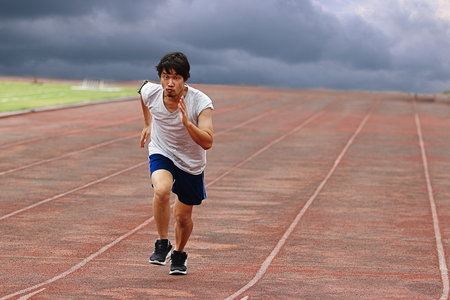 Young Asian runner running on track with weather storm background.