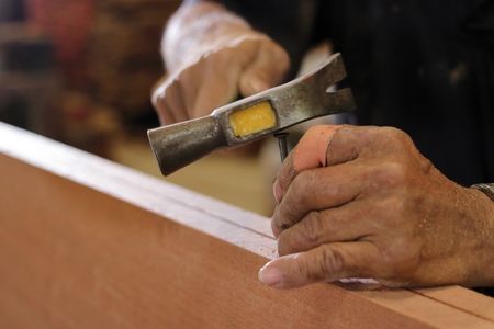 Close up hammer and nail using by carpenter on wooden board. Selective focus and shallow depth of...