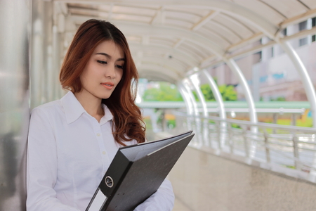 Portrait of young attractive Asian businesswoman holding document folder at pathway of outside office with copy space background.の写真素材