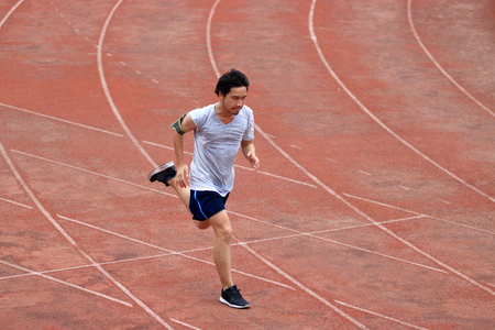 Athlete Asian man running on racetrack in stadium. Healthy active lifestyle concept.