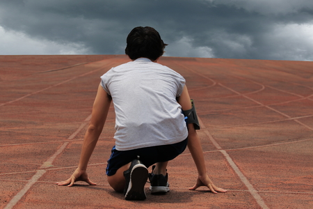 Back view of athlete man ready to run on track in the stadium against the dark cloudy background.の写真素材