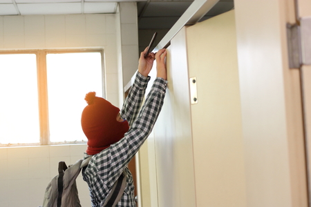 Side view of masked thief sneaking and taking a photo with mobile smart phone in toiletの写真素材