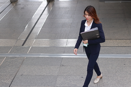 Aerial view of young attractive Asian business woman holding document folder and walking on flooring in the city against copy space background.の写真素材