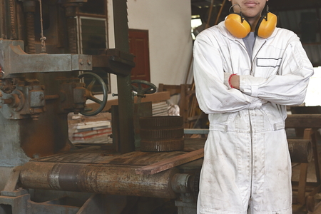 Portrait of confident young worker in white uniform standing and cross one's arms over the chest with band saw machine background.の写真素材
