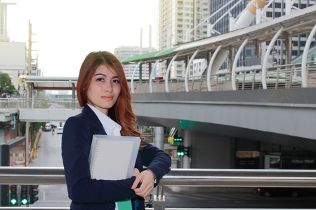 Portrait of young attractive Asian business woman standing and holding ring binder at the downtown city background.の写真素材