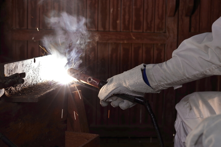 Hands of professional industrial welder man with torch and protective gloves welding metal steel with spark in the factory.の写真素材