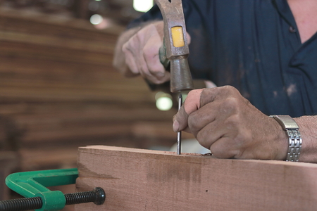 Selective focus and shallow depth of field. Hands of senior worker hitting nail on a wooden board...