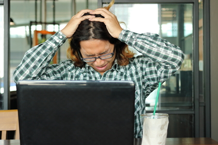 Stressed young Asian business man with hands on head feeling tired against his work in office....