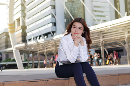 Portrait of leader young Asian business woman thinking and sitting on stairway in urban building background.の写真素材