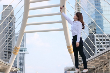 Side view of beautiful young Asian woman taking a selfie photo at urban city against copy space...