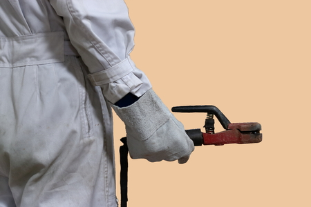 Back view of professional welder worker in white uniform holding arc welding torch in his hands on isolated background.の写真素材