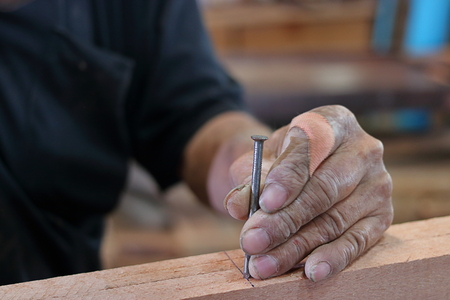 Hands senior carpenter holding nail on wooden piece with copy space.の写真素材
