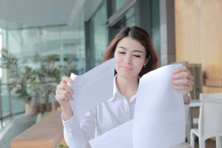 Portrait of beautiful young Asian business woman holding charts or paperwork on her hand on the desk in office.の写真素材