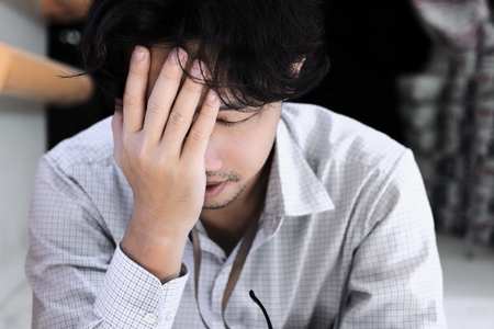 Frustrated stressed young Asian business man with hands of forehead feeling tired or exhausted with job.の写真素材